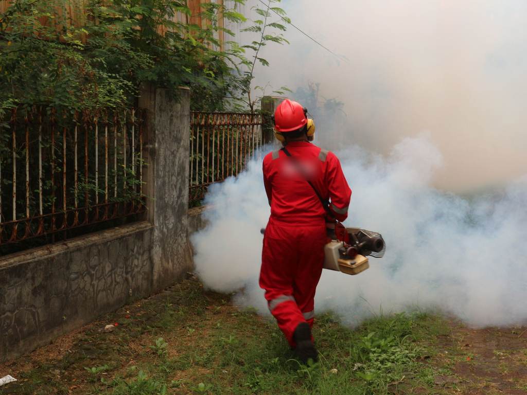 Pest control technician in a red suit fogging a yard
