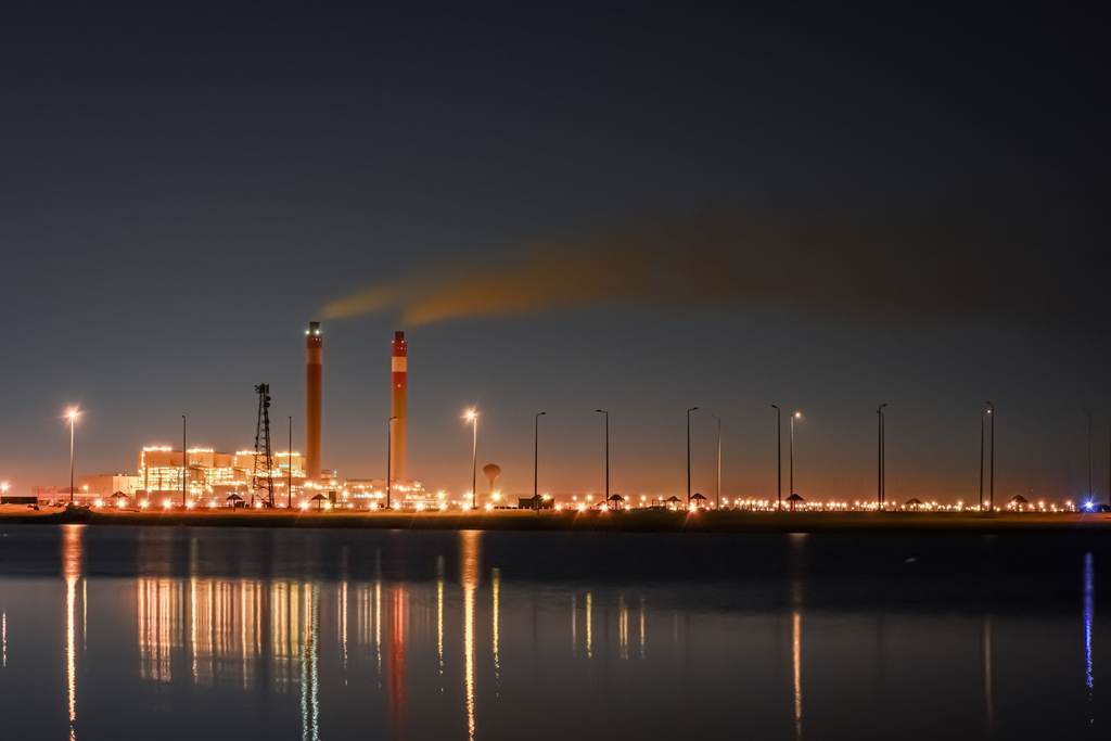 Industrial plant lights reflected in still water at blue hour